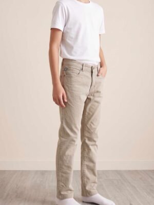 Jeune garçon portant un pantalon chino beige Cyrillus avec un t-shirt blanc, vue de profil.